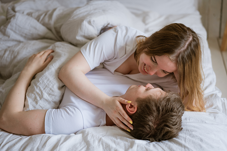 Lovely young caucasian couple on white blanket on white bed in room beds, looking into each others eyes in an embrace. Lovely couple romantic concept